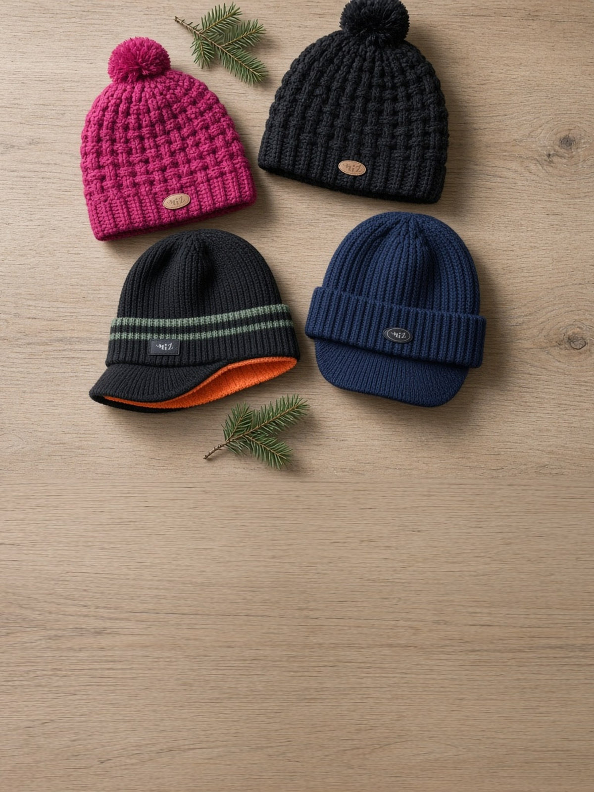 Four knit beanies on a light oak table: two pompom beanies and two ribbed beanies with a short visor